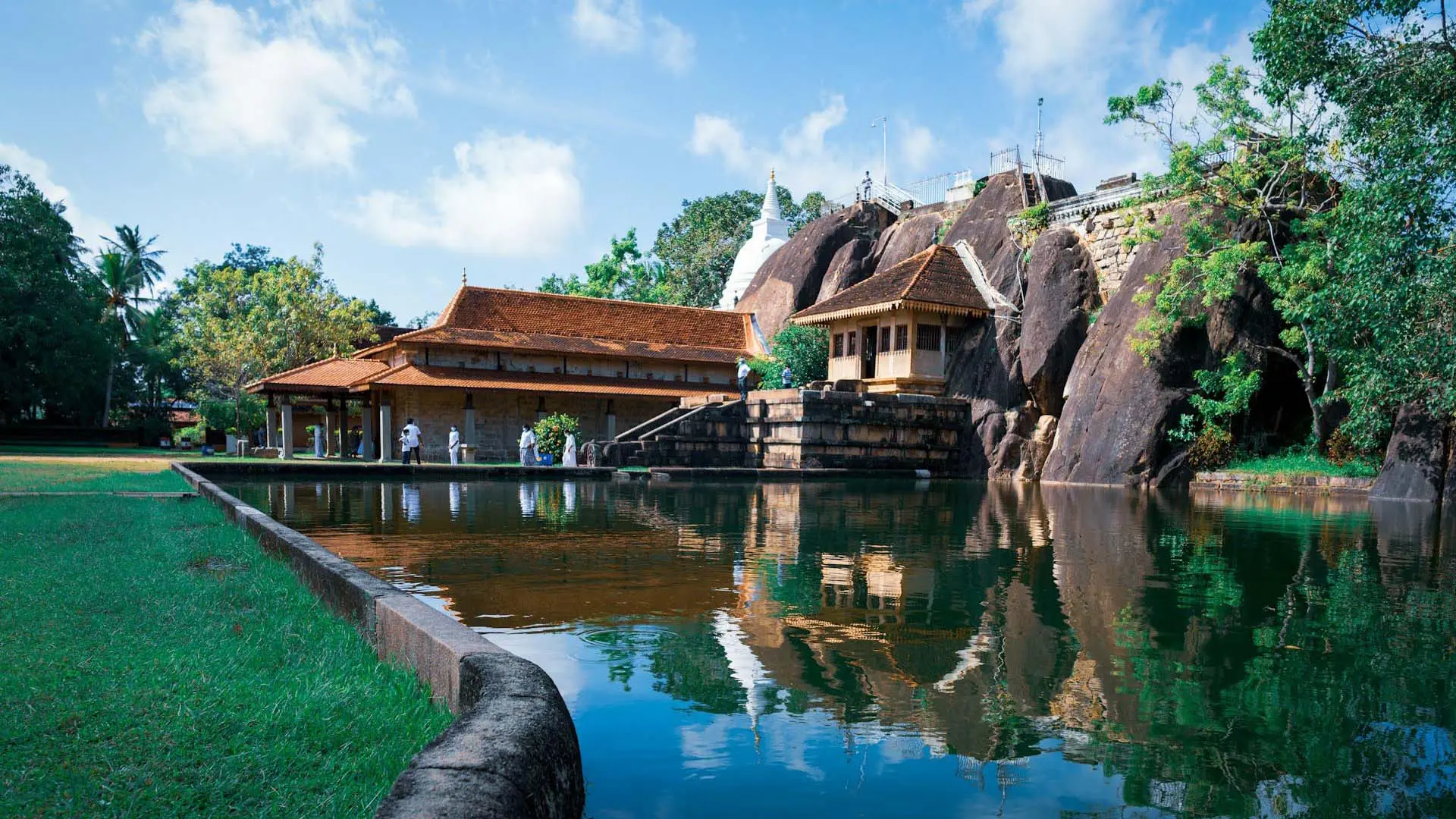 Serene Isurumuniya temple with traditional architecture reflected in a pond amidst lush surroundings.