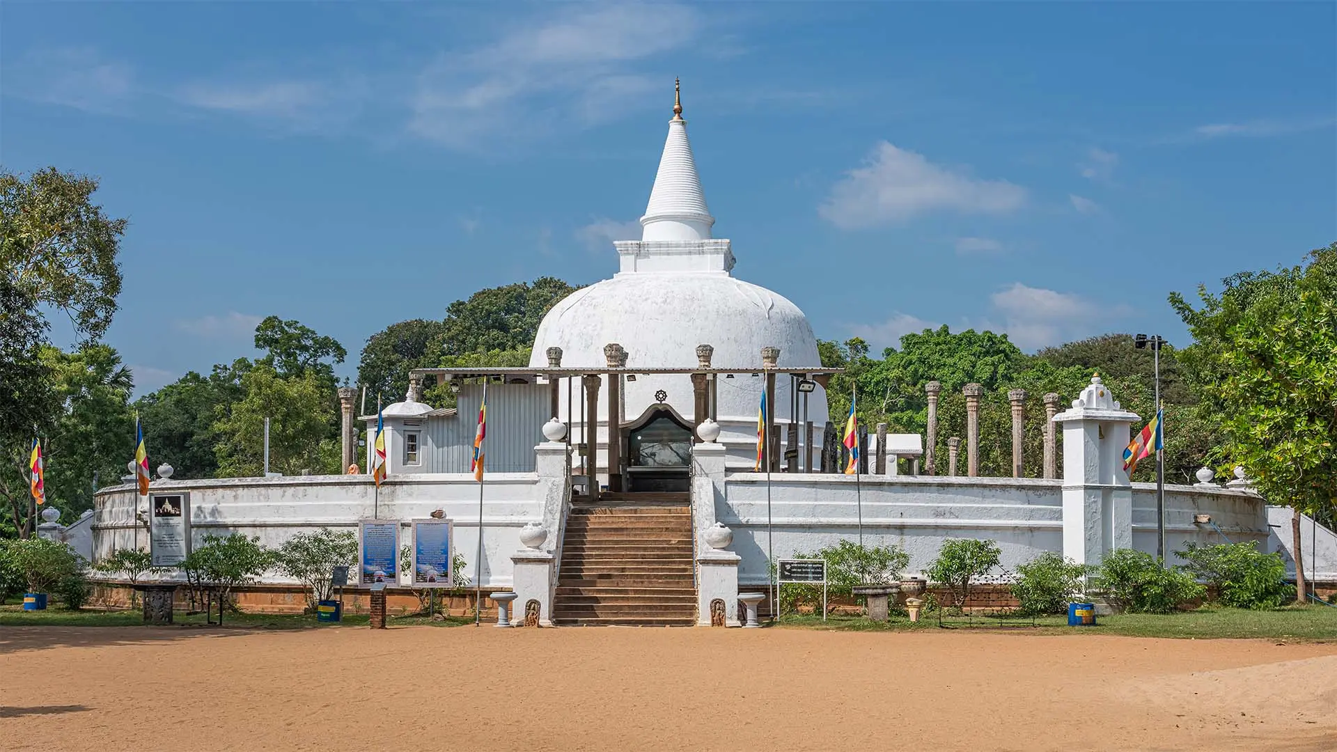 Lankarama stupa with golden spire and ancient columns amidst lush greenery under a clear blue sky.