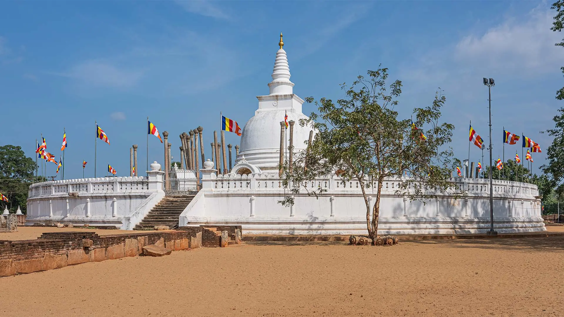 Thuparamaya stupa with golden spire and ancient columns under a clear blue sky.