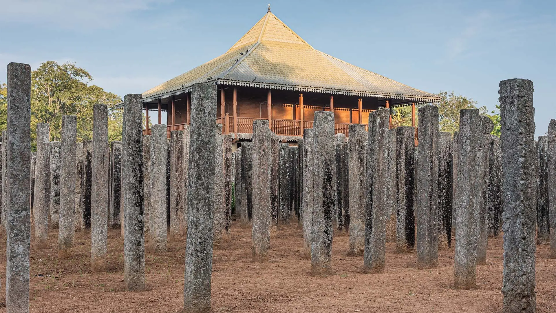Lovamahapaya with a wooden structure on ancient stone pillars under a clear sky.