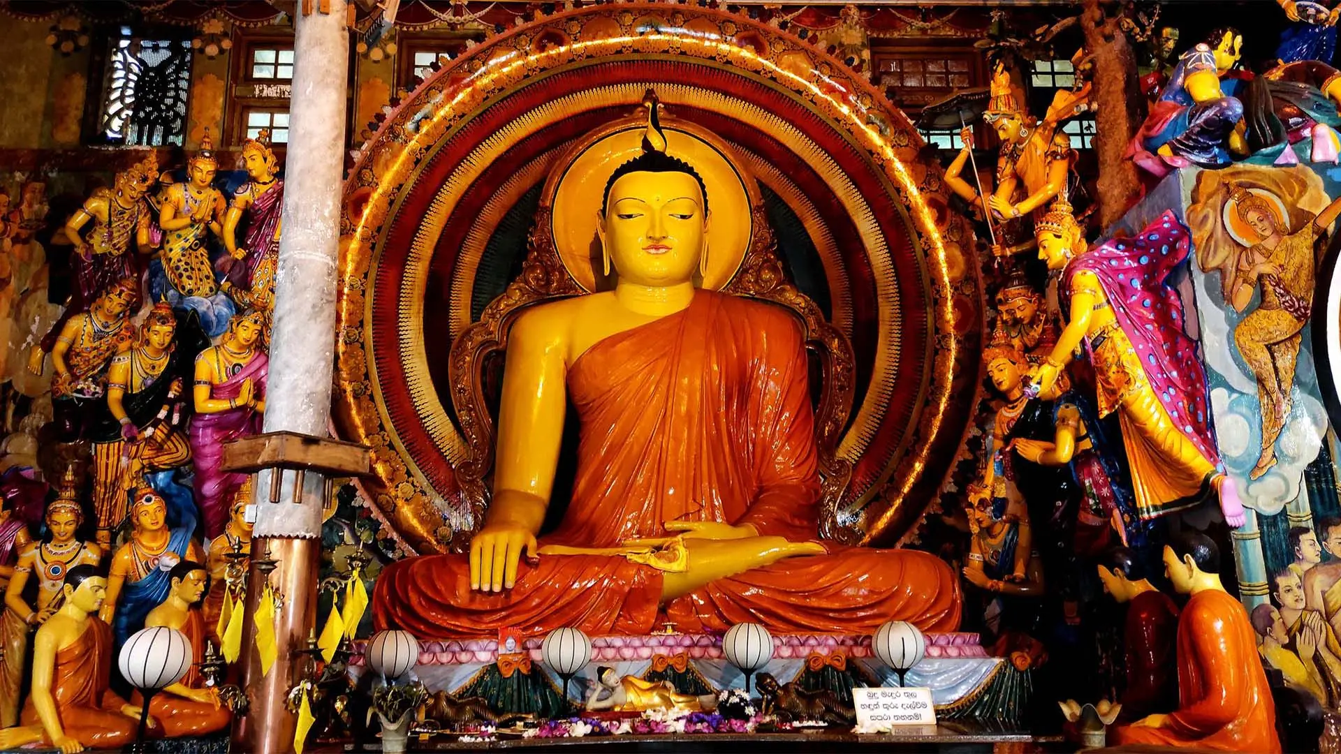 Interior of Gangaramaya Temple featuring a large golden Buddha statue with intricate decorations, colorful statues, and offerings.