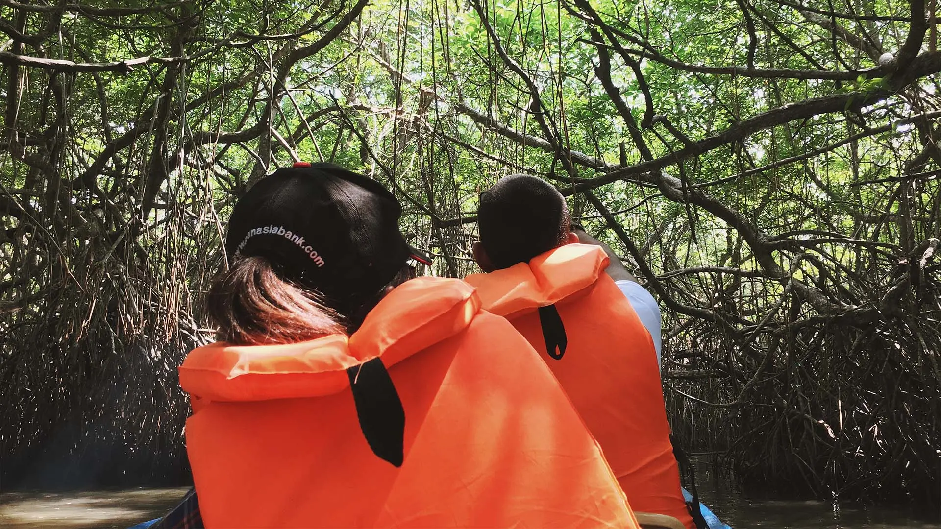 Madu River boat ride with a couple in orange life jackets navigating through lush mangrove forests.