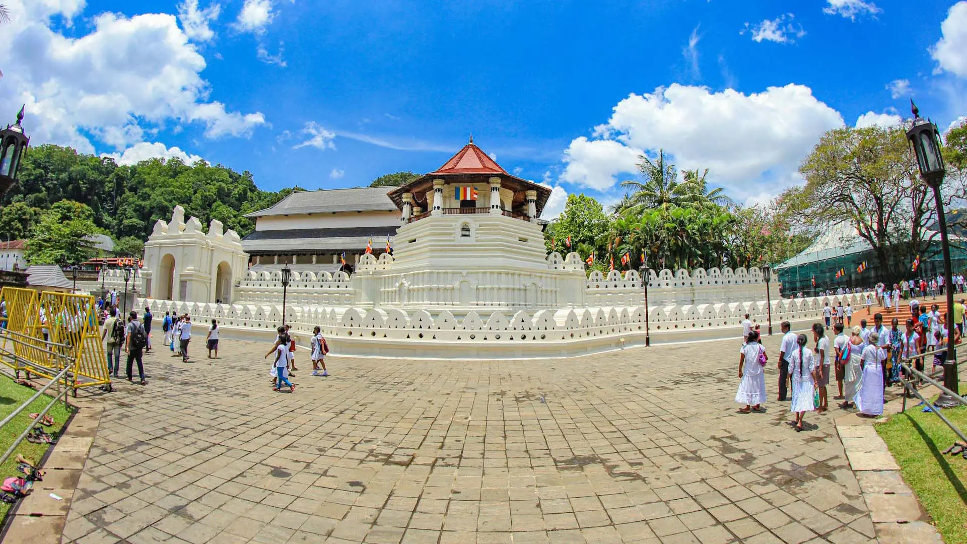 Ornate Temple of the Sacred Tooth Relic with white walls and visitors under a bright blue sky.