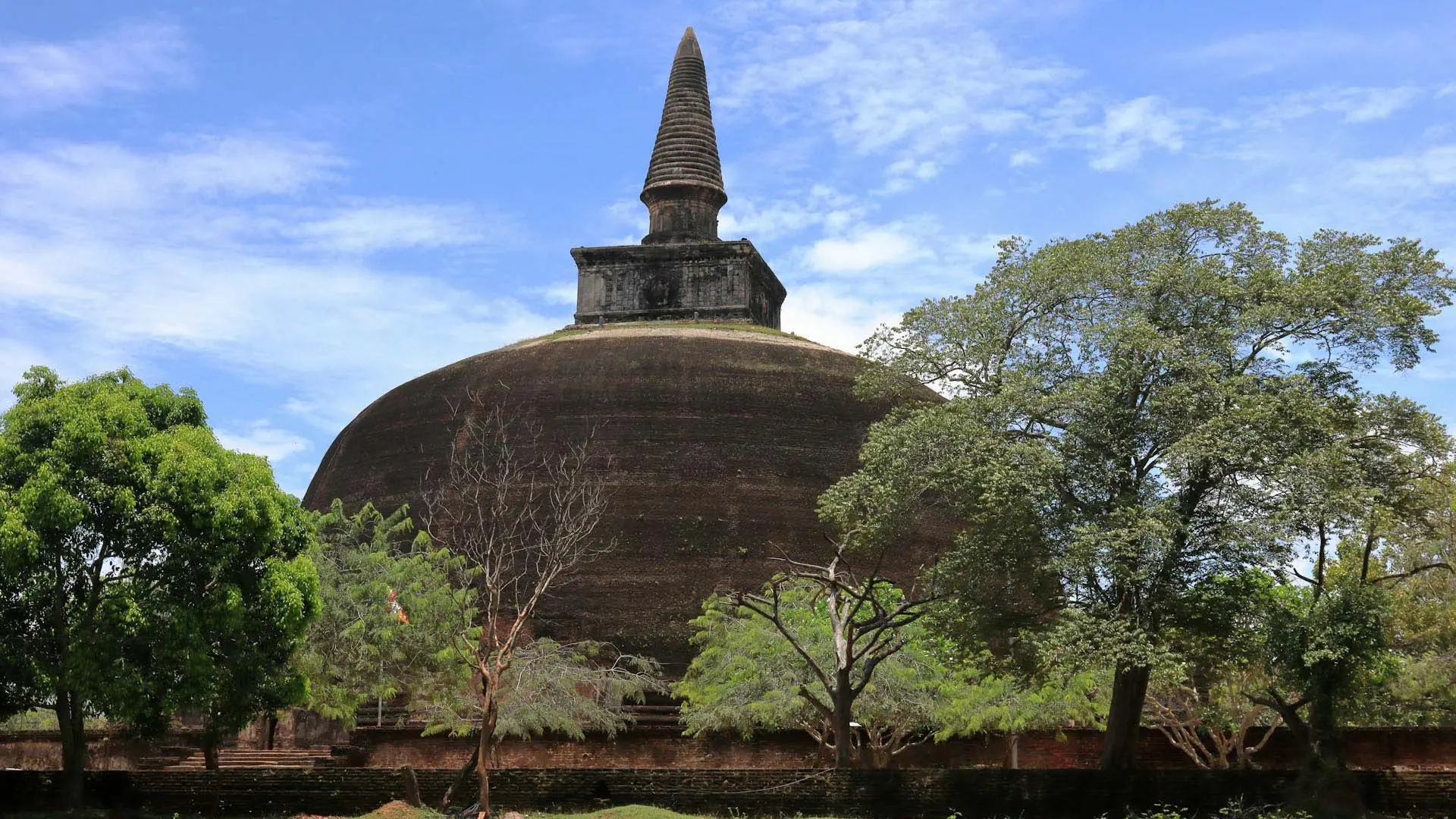 Ancient Rankoth Vehera stupa and spire amidst lush greenery under a clear blue sky.