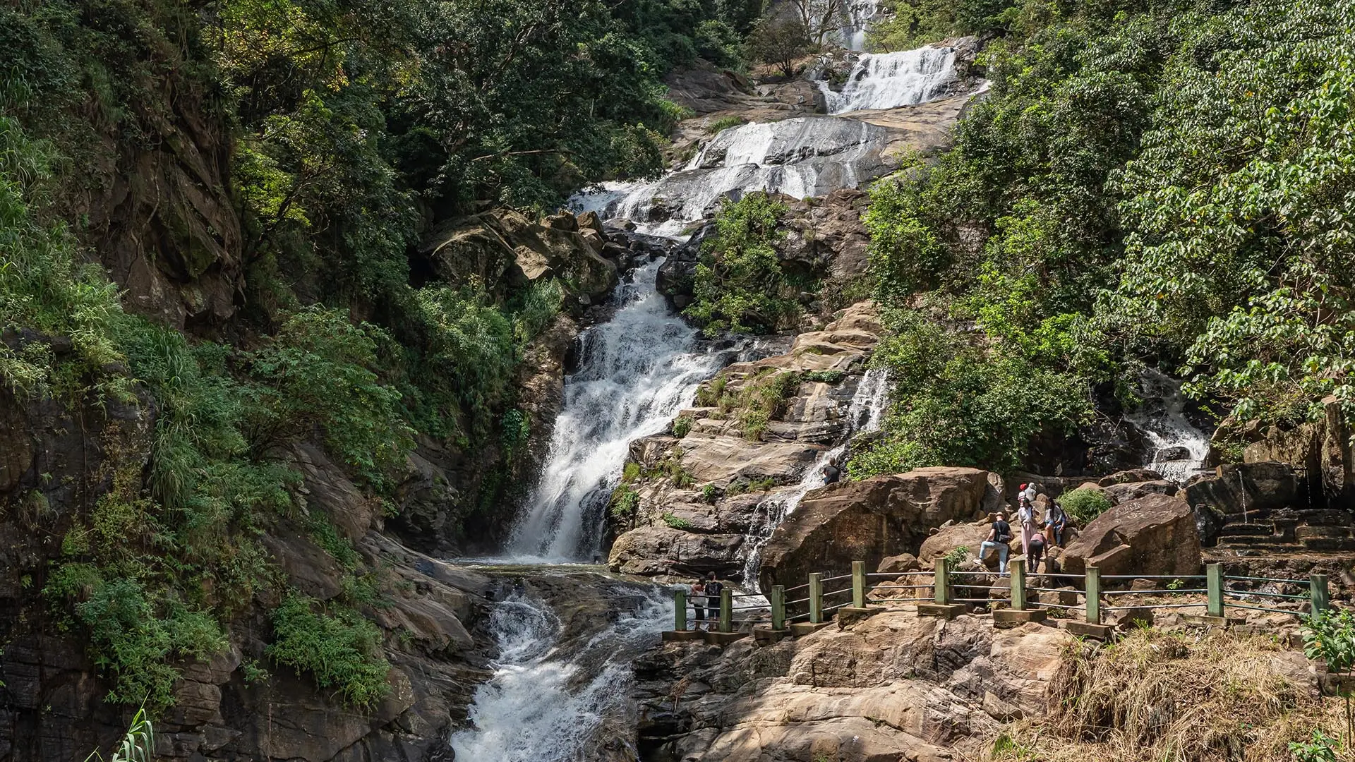 Ravana Falls surrounded by lush greenery and rocky terrain, featuring visitors on a viewing platform.
