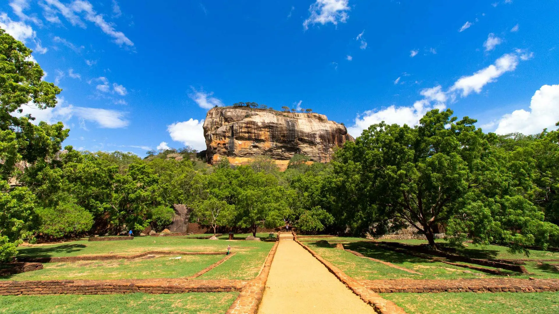 Majestic Sigiriya Rock with ancient ruins and lush greenery under a clear blue sky.